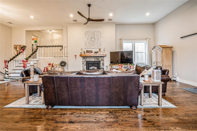 living room featuring a stone fireplace, a baseboard heating unit, ceiling fan, and dark hardwood / wood-style floors