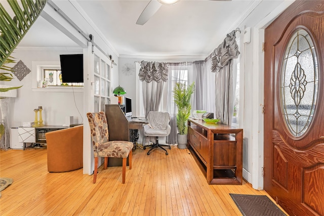 living area with a barn door, ceiling fan, crown molding, and light wood-type flooring