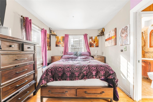 bedroom featuring connected bathroom, radiator heating unit, multiple windows, and light hardwood / wood-style flooring