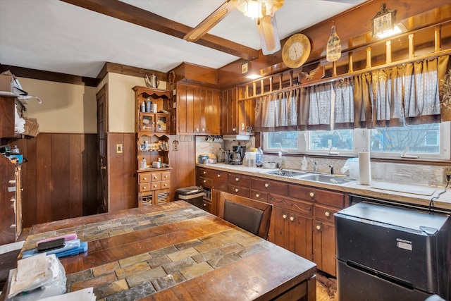 kitchen with beam ceiling, sink, ceiling fan, fridge, and wooden walls