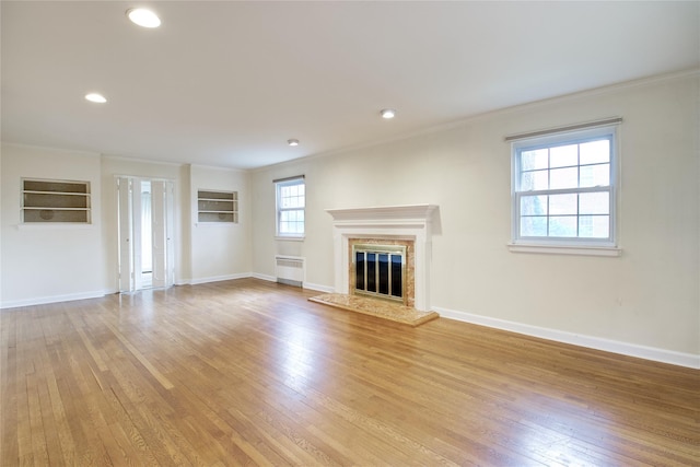 unfurnished living room featuring a wealth of natural light, light hardwood / wood-style floors, radiator, and crown molding