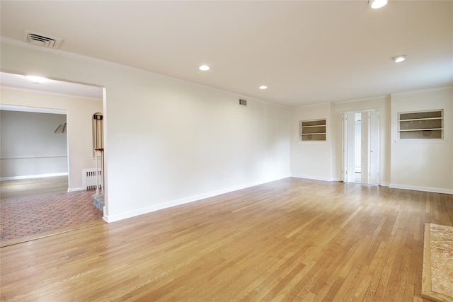 empty room featuring radiator heating unit, light wood-type flooring, and ornamental molding