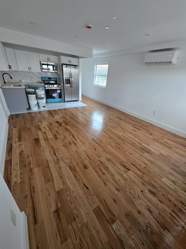 unfurnished living room with a wall mounted AC, sink, and light hardwood / wood-style floors