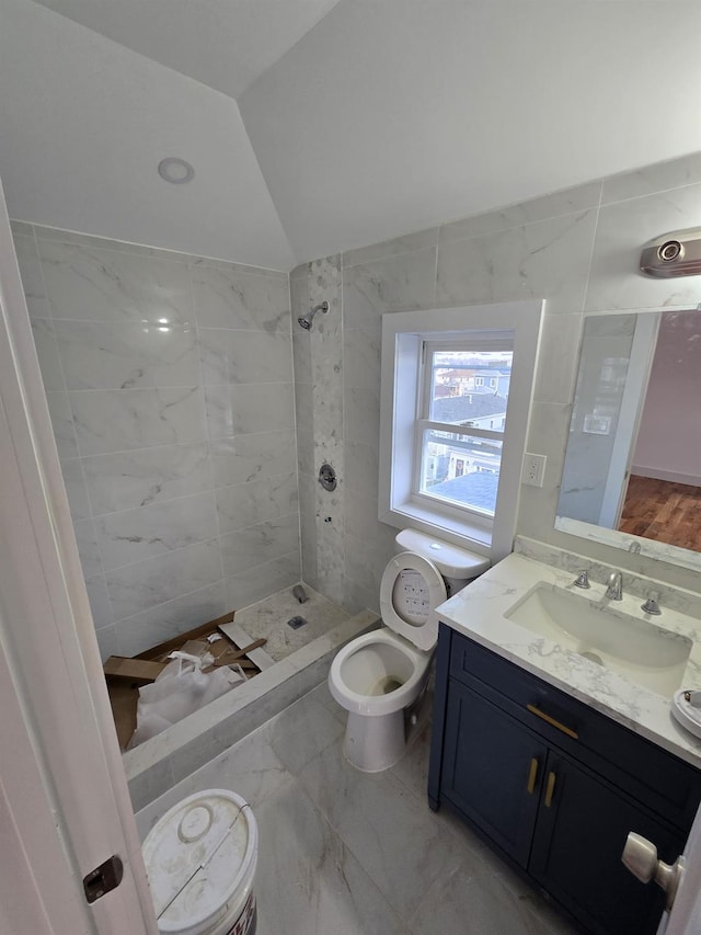 bathroom featuring vanity, toilet, tiled shower, and vaulted ceiling