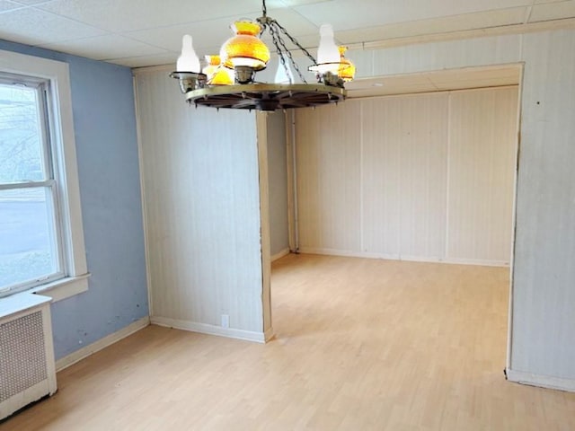 unfurnished dining area with a notable chandelier, a drop ceiling, radiator heating unit, and wood-type flooring