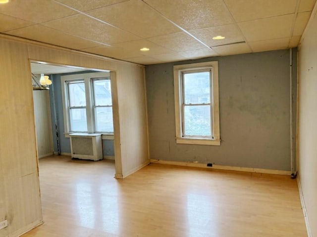 unfurnished room with a chandelier, a drop ceiling, and light wood-type flooring