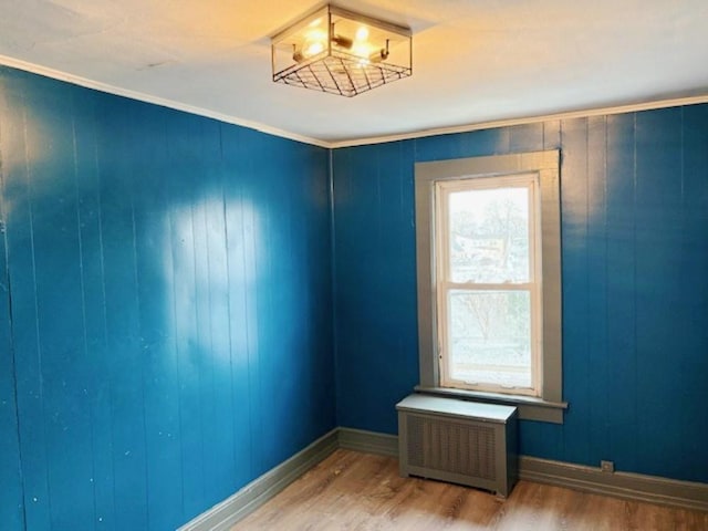 empty room featuring ornamental molding, radiator heating unit, wood walls, and hardwood / wood-style flooring