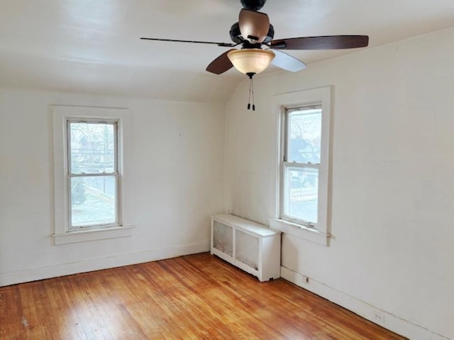 empty room featuring ceiling fan, light wood-type flooring, vaulted ceiling, and radiator