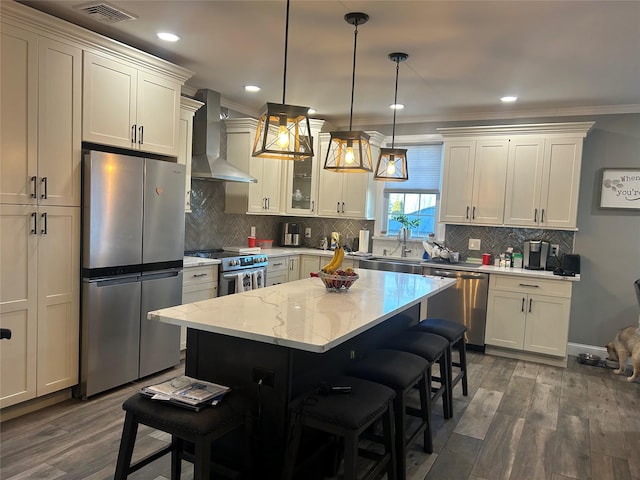 kitchen with pendant lighting, a center island, a breakfast bar area, wall chimney exhaust hood, and stainless steel appliances