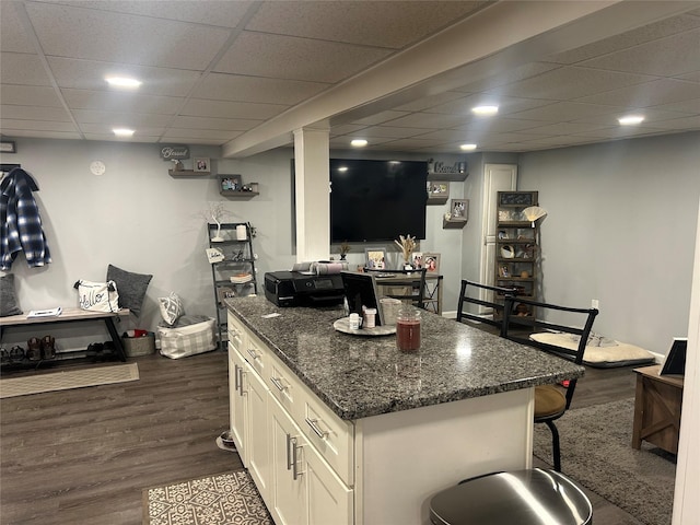 kitchen featuring a kitchen bar, dark wood-type flooring, dark stone countertops, a center island, and white cabinetry