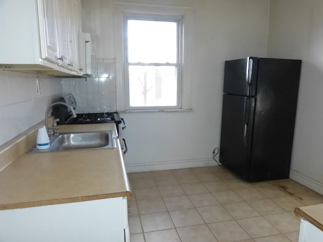 kitchen with black refrigerator, backsplash, white cabinets, and sink