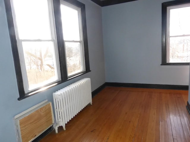 spare room featuring a healthy amount of sunlight, wood-type flooring, and radiator heating unit