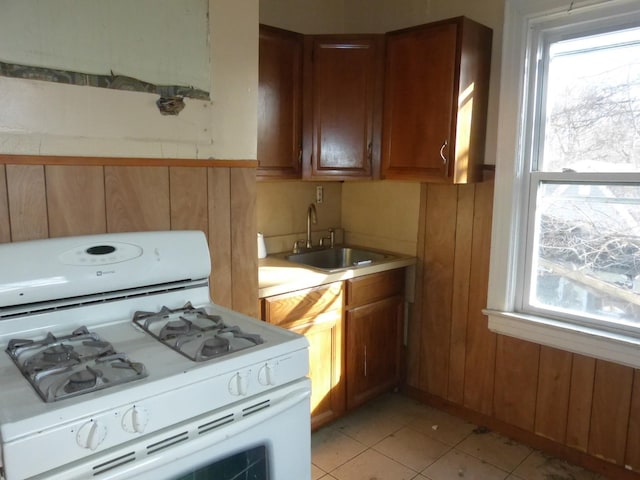 kitchen featuring wood walls, white range with gas stovetop, and sink