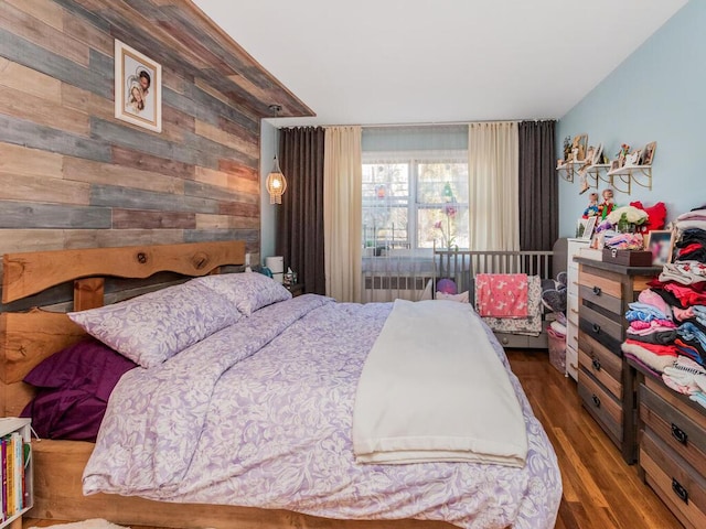 bedroom featuring radiator heating unit, dark hardwood / wood-style flooring, and wood walls