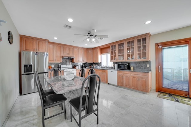 kitchen featuring a center island, stainless steel appliances, dark stone countertops, tasteful backsplash, and ceiling fan