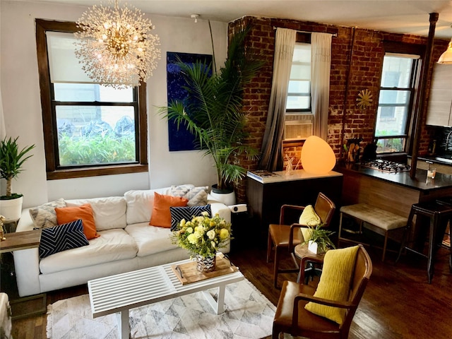 living room with a healthy amount of sunlight, dark hardwood / wood-style flooring, a notable chandelier, and brick wall