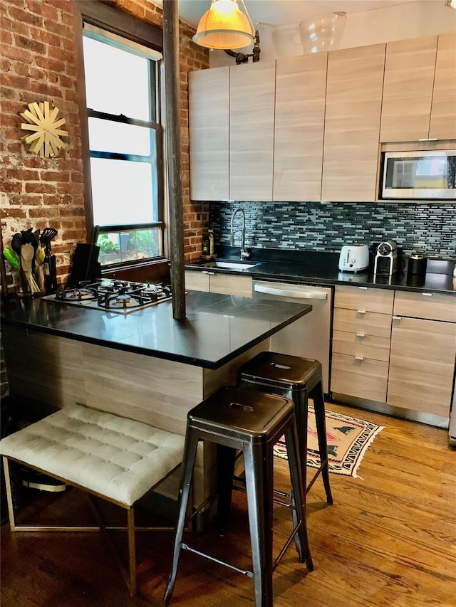 kitchen with sink, stainless steel appliances, brick wall, a breakfast bar, and light wood-type flooring