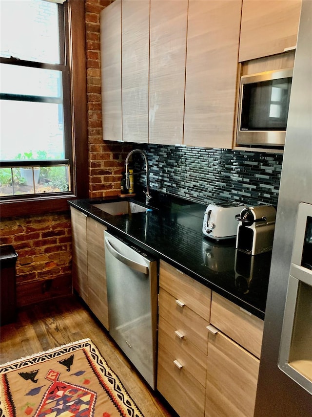 kitchen with backsplash, stainless steel appliances, sink, hardwood / wood-style flooring, and dark stone countertops