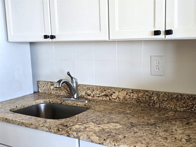 room details with sink, white cabinetry, stone counters, and decorative backsplash