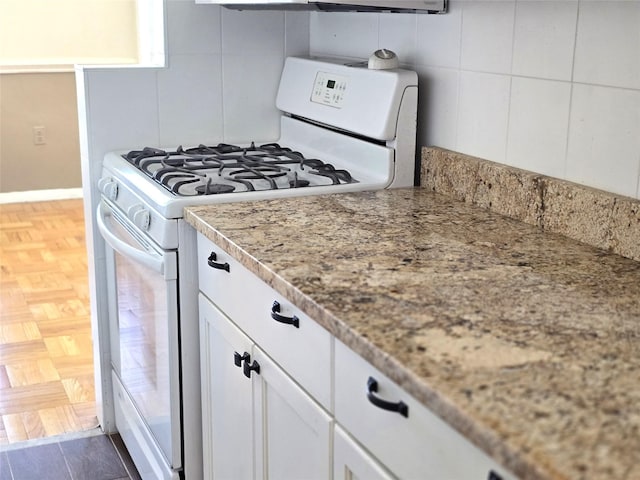 kitchen with white cabinets, dark wood-type flooring, tasteful backsplash, white gas range, and light stone counters