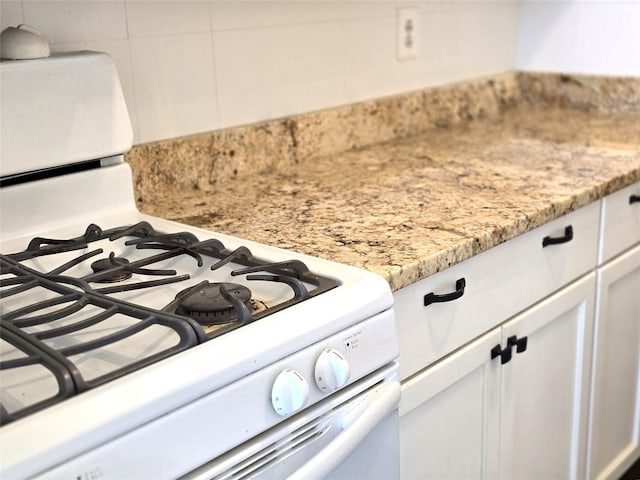 room details with light stone counters, white cabinets, and white gas stove