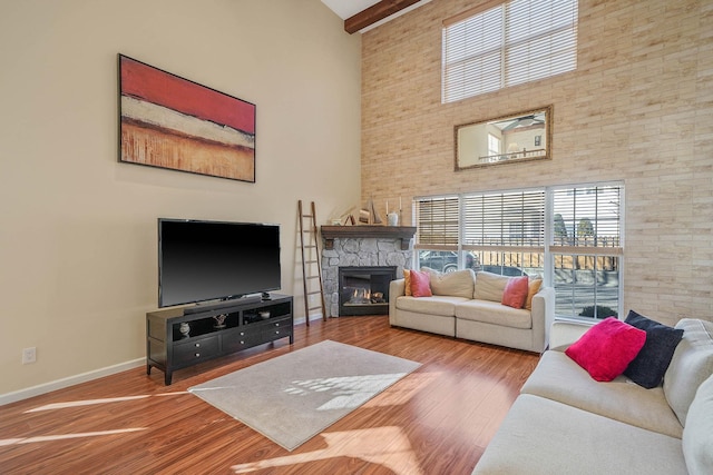 living room featuring a towering ceiling, hardwood / wood-style flooring, beam ceiling, and a stone fireplace