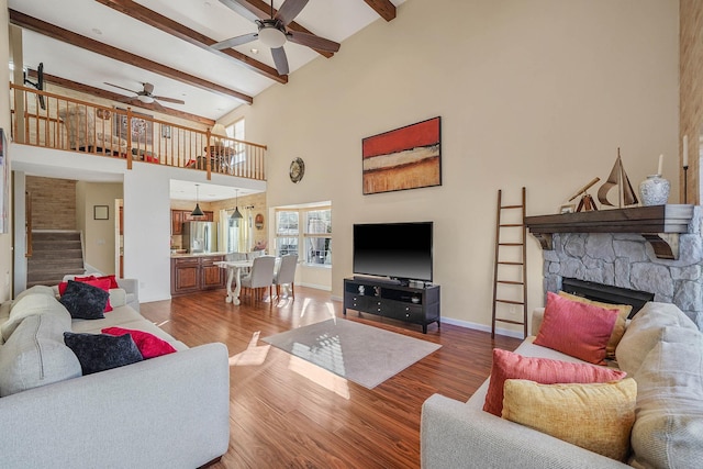 living room featuring hardwood / wood-style floors, a towering ceiling, ceiling fan, a fireplace, and beam ceiling