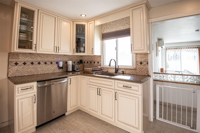 kitchen with cream cabinetry, stainless steel dishwasher, dark stone counters, and sink