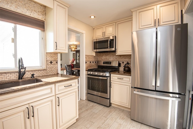 kitchen featuring dark stone counters, cream cabinets, stainless steel appliances, and sink