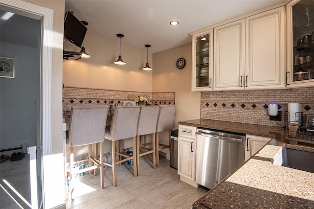 kitchen with hanging light fixtures, stainless steel dishwasher, decorative backsplash, dark stone countertops, and light wood-type flooring