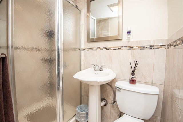 bathroom featuring sink, toilet, a shower with shower door, and tile walls