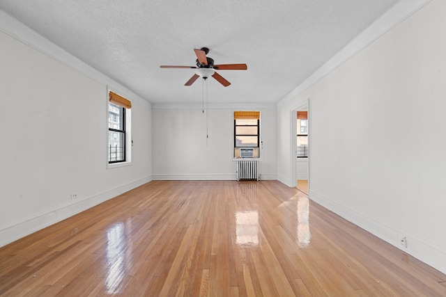 empty room featuring a textured ceiling, light hardwood / wood-style flooring, radiator, and ceiling fan