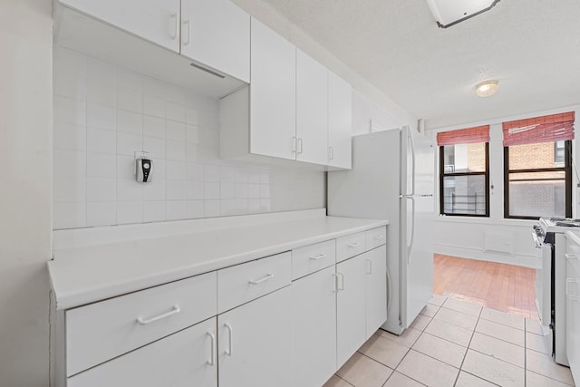 kitchen with backsplash, light tile patterned floors, white cabinets, and white appliances