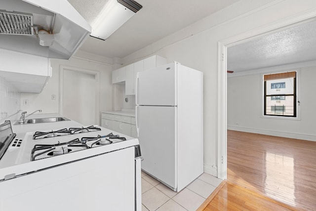 kitchen featuring a textured ceiling, white appliances, sink, light tile patterned floors, and white cabinetry