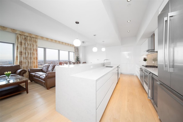 kitchen with appliances with stainless steel finishes, decorative backsplash, light wood-type flooring, hanging light fixtures, and sink