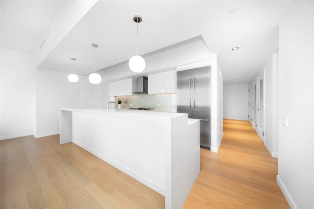 kitchen with light hardwood / wood-style floors, tasteful backsplash, built in fridge, hanging light fixtures, and wall chimney exhaust hood