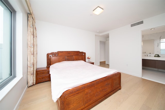 bedroom with ensuite bathroom and light wood-type flooring