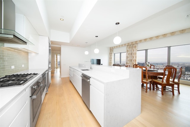 kitchen with wall chimney range hood, hanging light fixtures, white cabinets, and appliances with stainless steel finishes