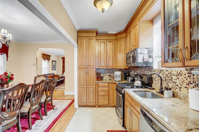 kitchen with sink, tasteful backsplash, light stone counters, crown molding, and appliances with stainless steel finishes