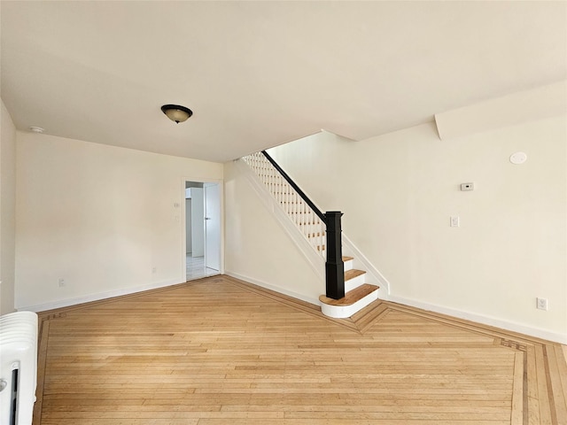 spare room with light wood-type flooring, baseboards, radiator, and stairway