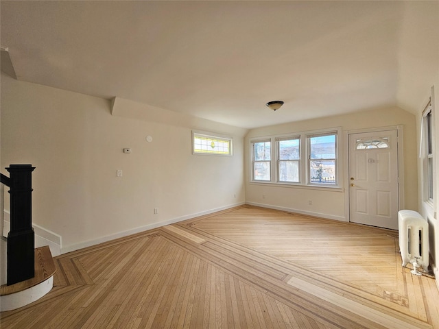 unfurnished living room with vaulted ceiling, light wood-style flooring, radiator heating unit, and baseboards