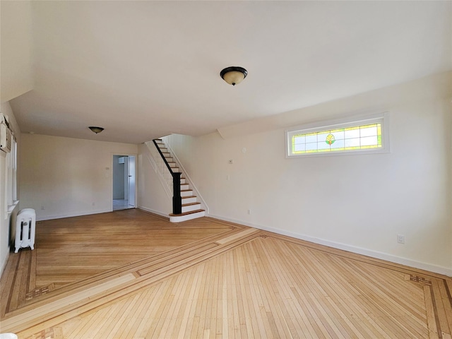 spare room with stairway, radiator heating unit, baseboards, and wood-type flooring