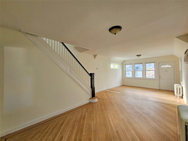 unfurnished living room featuring stairway, baseboards, light wood-style flooring, and radiator heating unit