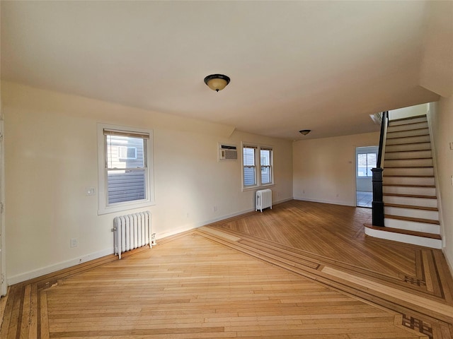 empty room featuring stairway, baseboards, radiator, and hardwood / wood-style flooring