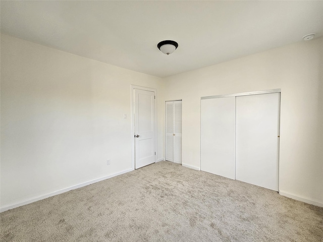 unfurnished bedroom with carpet flooring, baseboards, and multiple closets