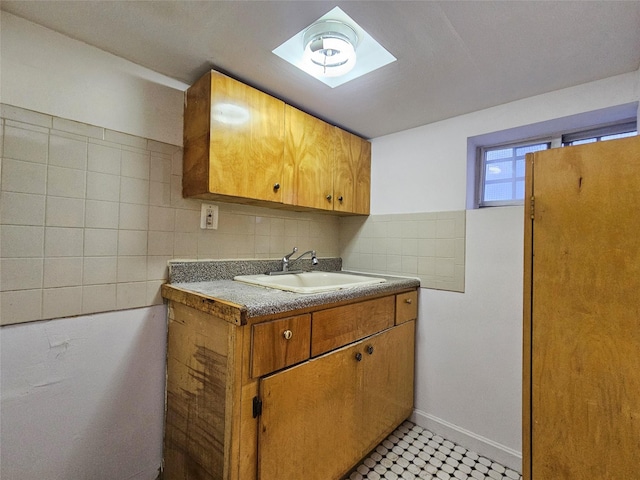 kitchen with backsplash, light floors, brown cabinetry, refrigerator, and a sink