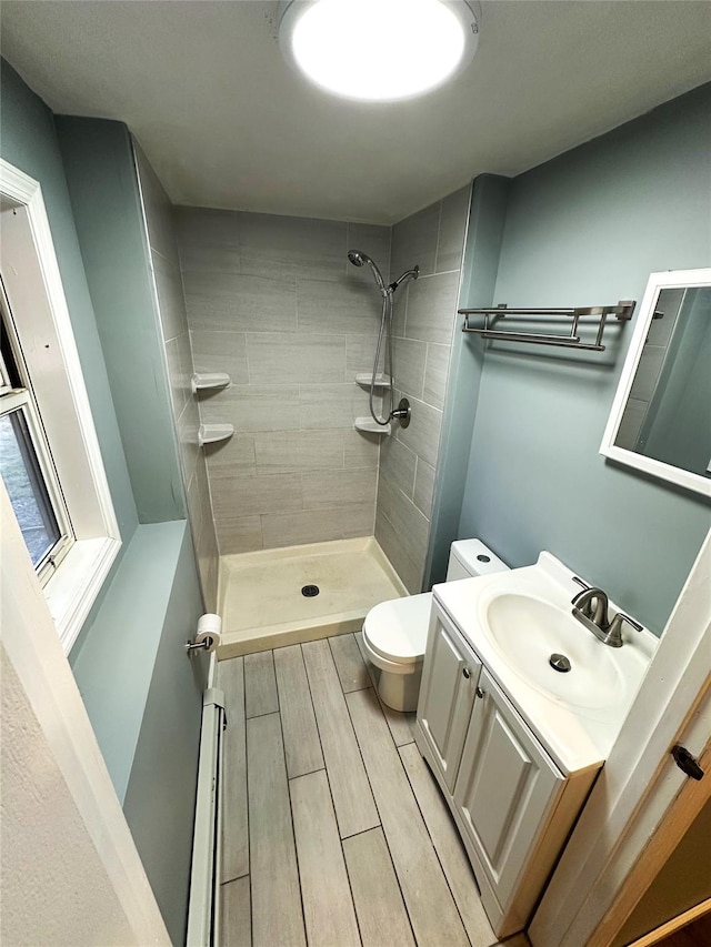 bathroom with toilet, vanity, a baseboard heating unit, and tiled shower