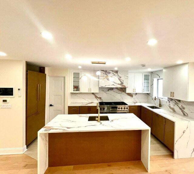 kitchen featuring sink, white cabinets, stainless steel stove, light stone counters, and a kitchen island