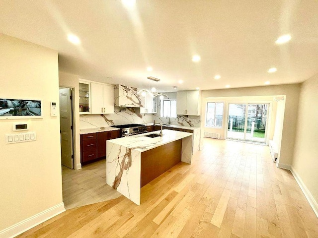 kitchen featuring a center island with sink, decorative backsplash, sink, white cabinetry, and wall chimney range hood