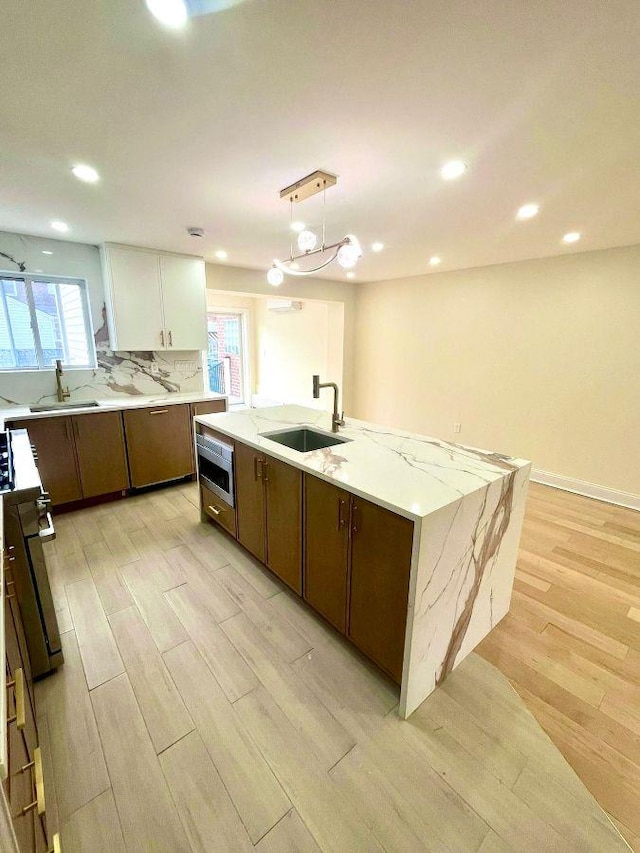 kitchen with decorative light fixtures, a kitchen island with sink, white cabinets, appliances with stainless steel finishes, and sink